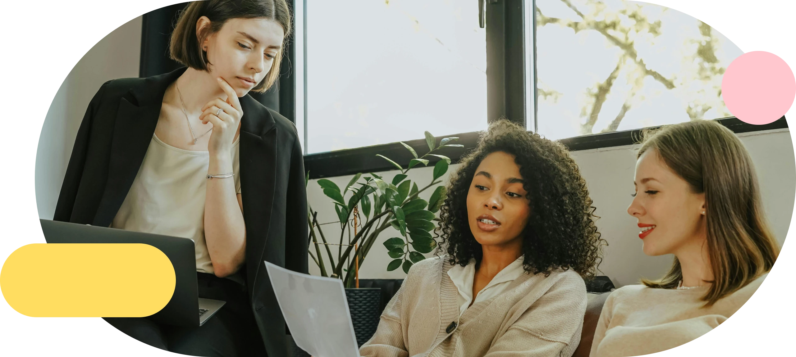 Three women in conversation on a couch, one holding a laptop and one holding a document