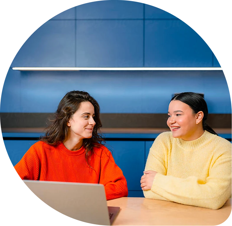 Two women at a table with a laptop, smiling and talking